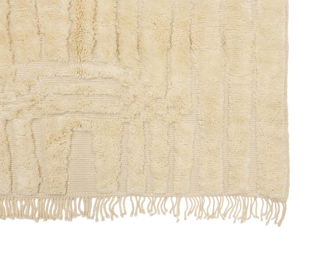 A close-up of a beige woven rugs corner reveals its fringed edges and intricate textured pattern, effortlessly enhancing the warmth and style of any space.