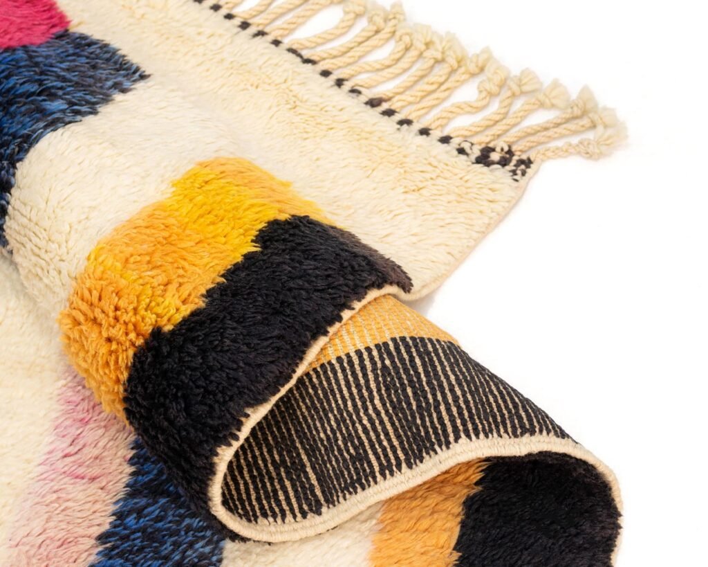 A vibrant, woven rug with blue, yellow, pink, and black stripes features fringe on the ends. Its partially folded to highlight its pattern and depth.