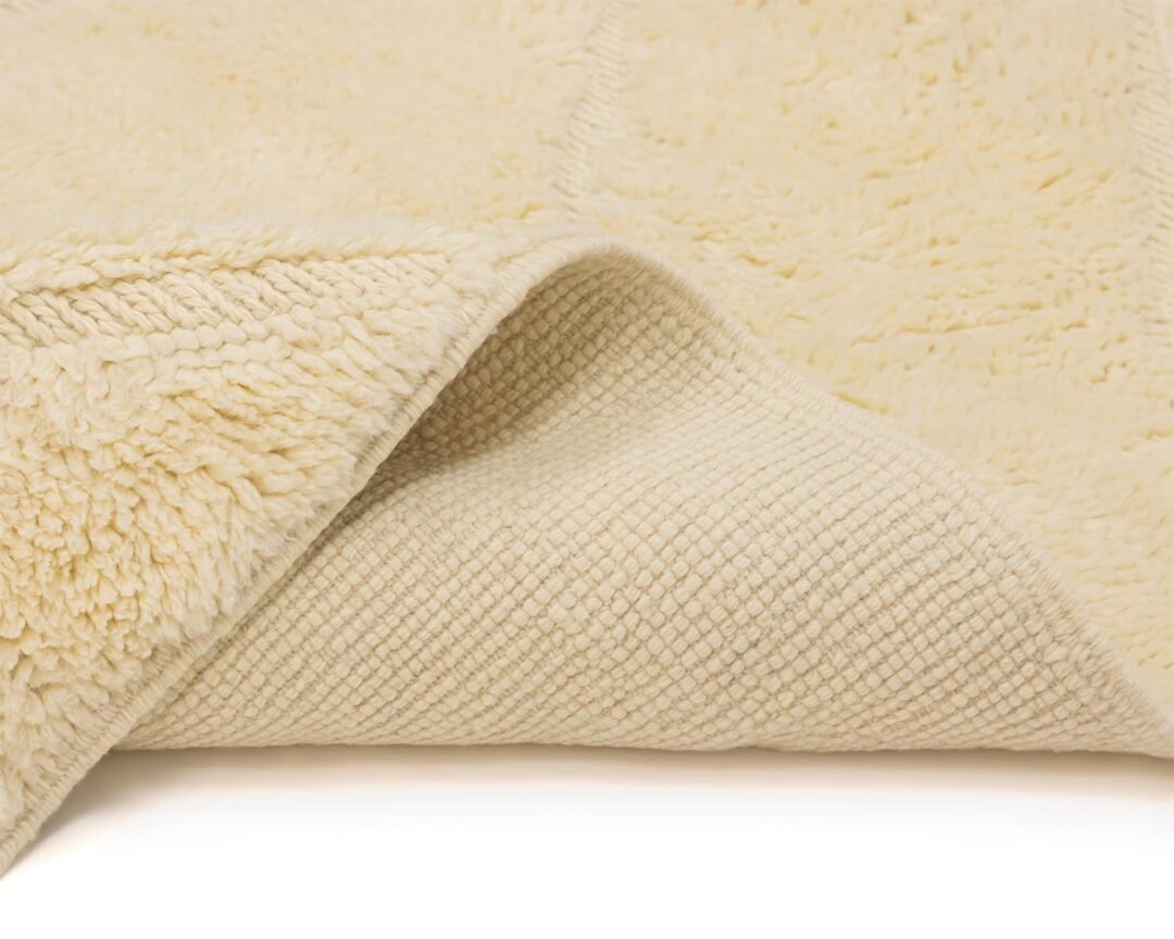 A close-up view reveals a white, textured woolen fabric with a soft fluffy side and a grid-patterned underside. This versatile material, slightly folded, showcases its dual textures beautifully.