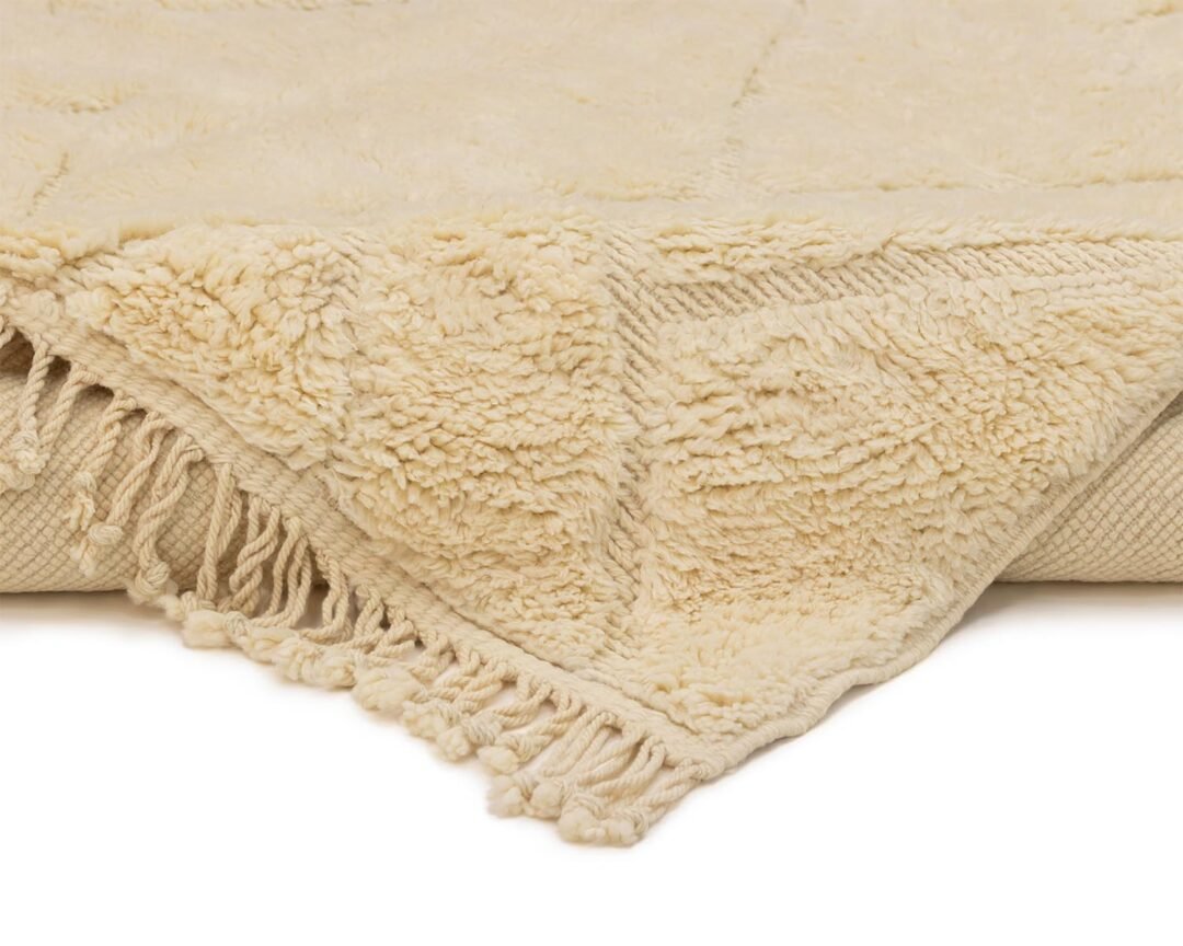 Close-up of an artisanal rugs cream-colored textured corner with fringed edges, showcasing detailed woven patterns.