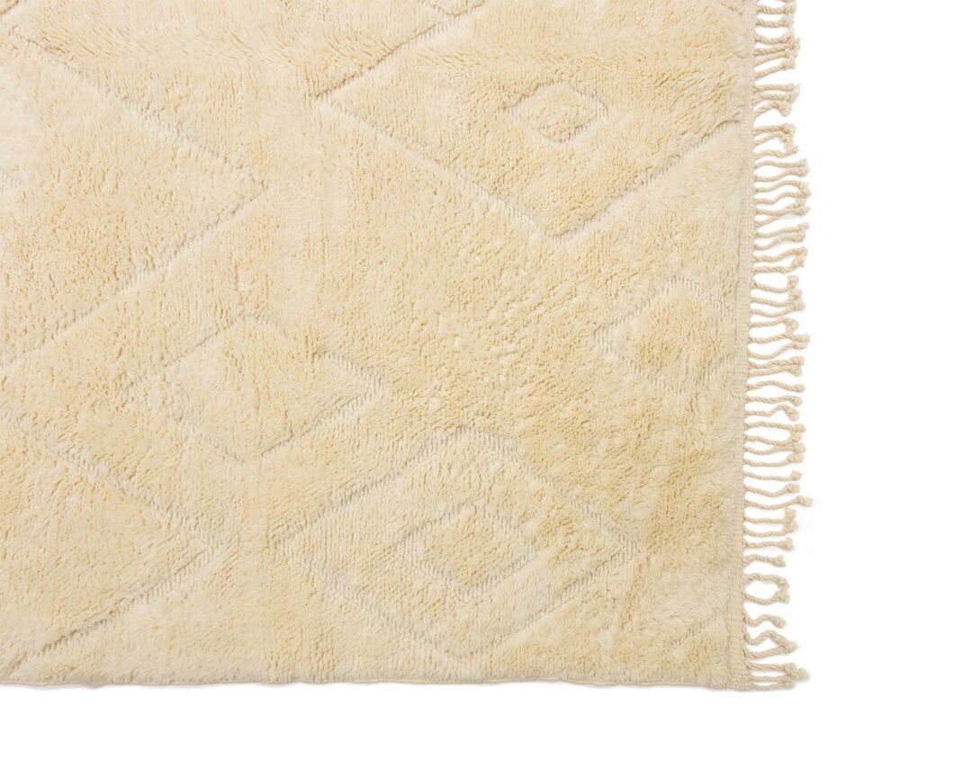 An artisanal rug in beige showcases a subtle diamond pattern and fringed edges on one side, exuding an authentic Moroccan touch.