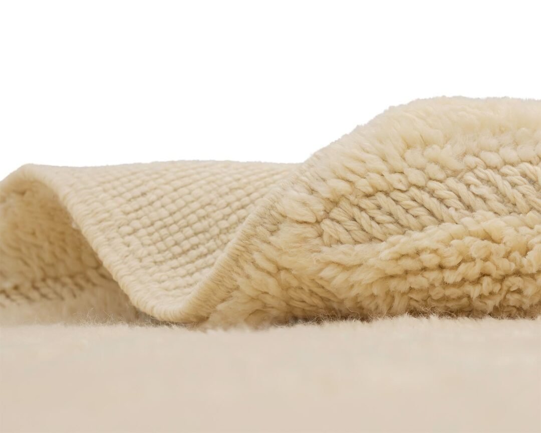 Close-up of a folded beige woolen artisanal rug with a textured knit pattern, showcasing soft fibers and an edge detail.