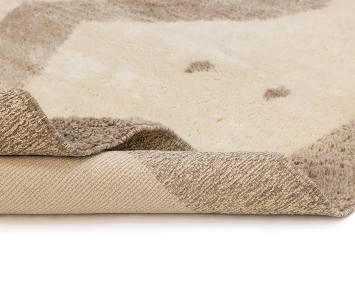 A close-up of a beige and brown area rug features a textured edge folded over, revealing its non-slip backing. The intricate design enhances any rooms elegance while ensuring safety with its sturdy grip.