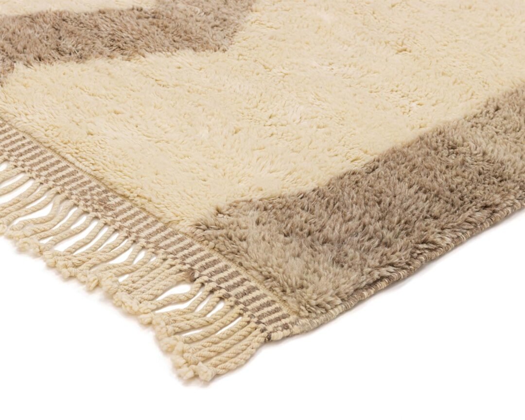 A beige and brown fringed rug, boasting a plush, fluffy texture, is showcased with alternating color bands. Some stripes evoke the cozy vibe of macramé, enhancing its layered appeal.