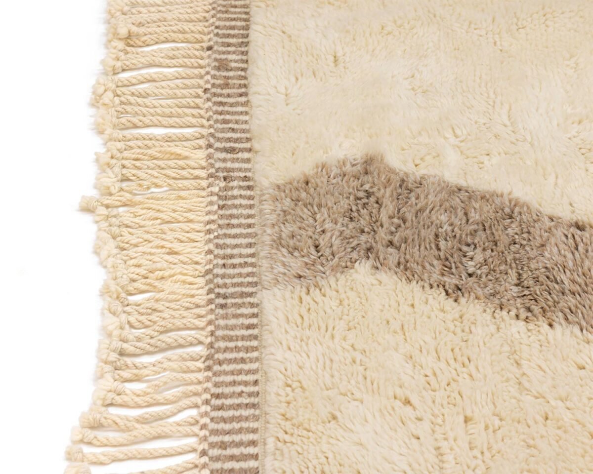 Close-up of a beige and brown rug with fringe detailing on one edge. The textured zigzag pattern adds a touch of rustic charm, perfect for a cozy living room or study.