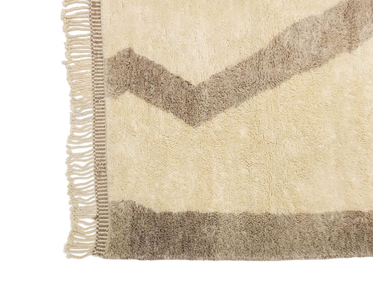 A textured rug corner with a fringed edge showcases a geometric zigzag pattern in earthy beige and brown tones.