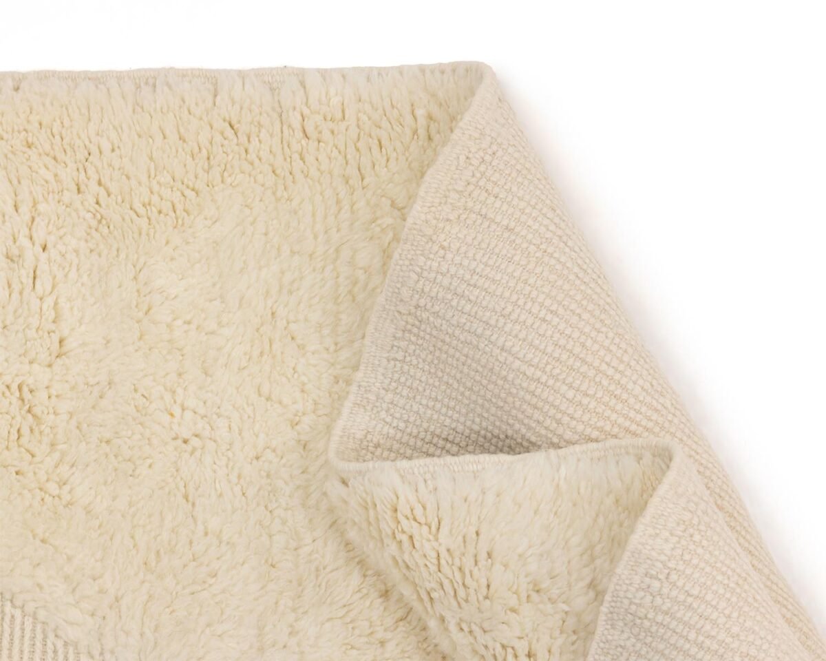 Close-up view of a beige rug displaying its plush surface and intricate woven underside, with corners gently folded over.