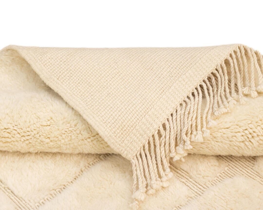 A cream-colored throw with a woven texture and fringe detailing on one edge, folded neatly for a cozy accent.