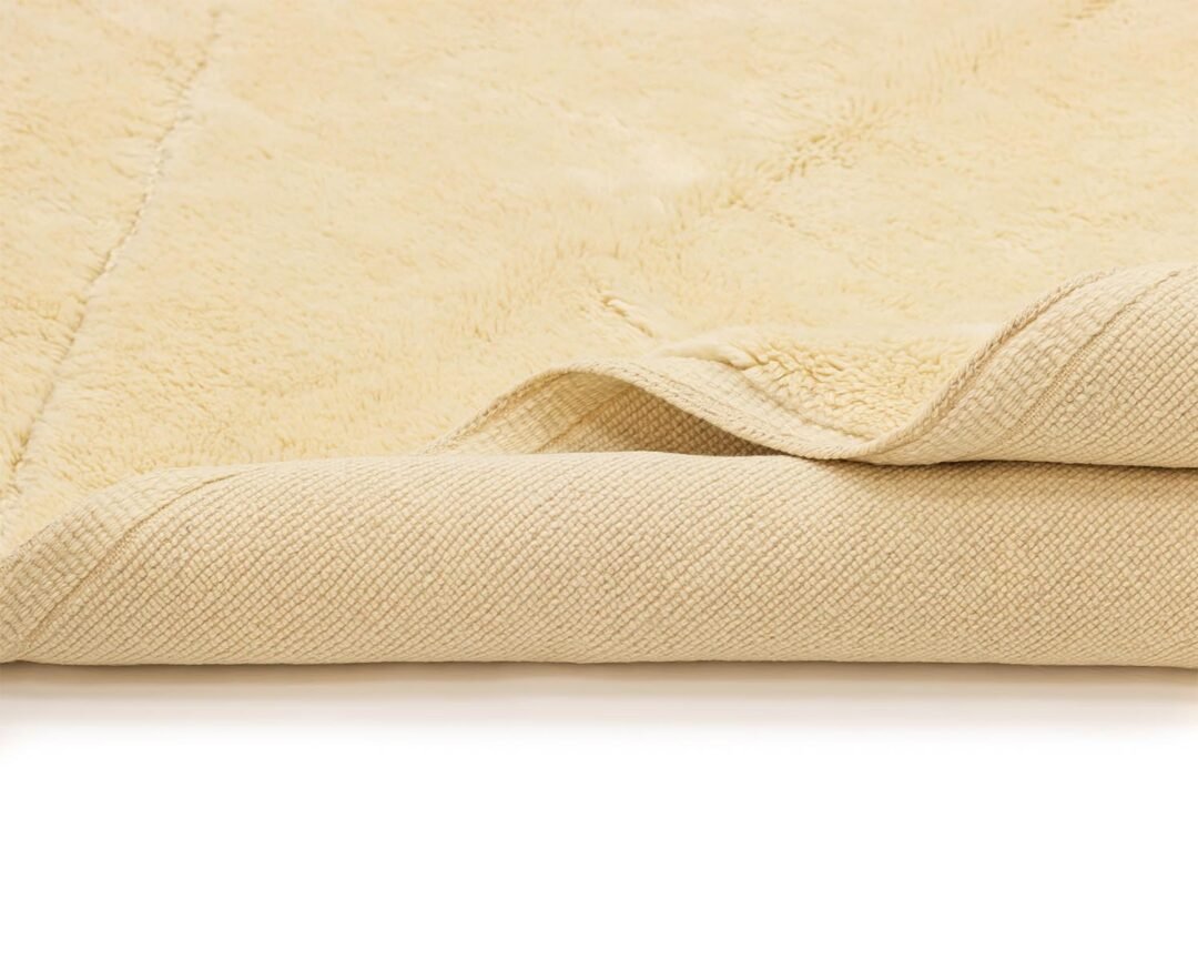 A cozy folded beige textile showcases a soft, fluffy surface paired with a finely woven underside.