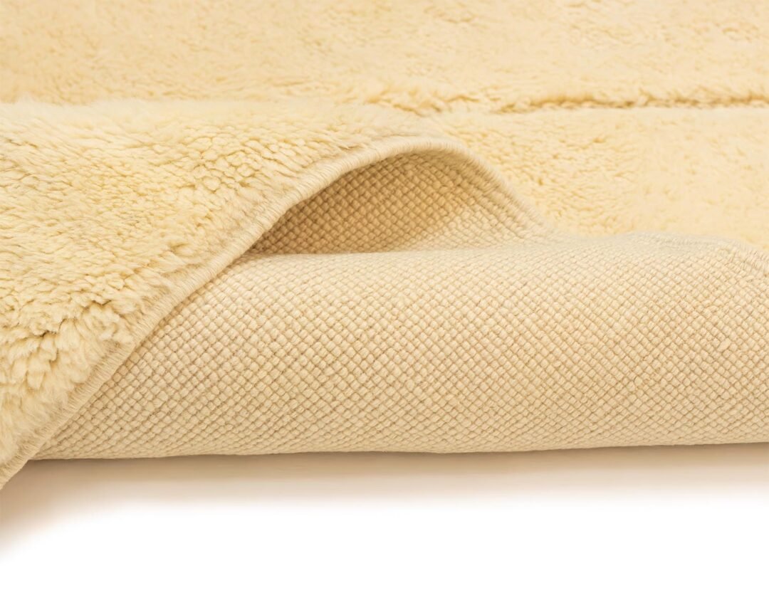 This cream-colored, textured fleece features a soft, fluffy side perfect for cozy evenings and a woven underside that adds durability. Its partially folded design invites you to wrap yourself in warmth and comfort.