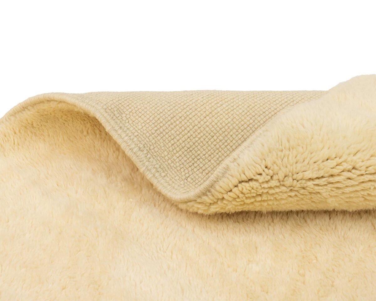 Close-up of a folded beige fleece with a textured underlayer and a fluffy outer surface, showcasing the contrast in textures.