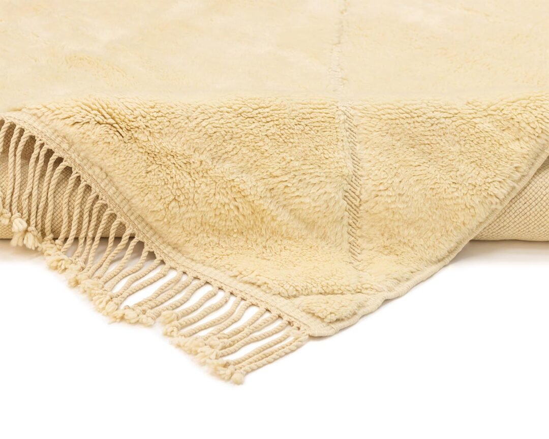 Close-up of a beige throw with fringed edges, showcasing its soft, textured surface and detailed fabric stitching.