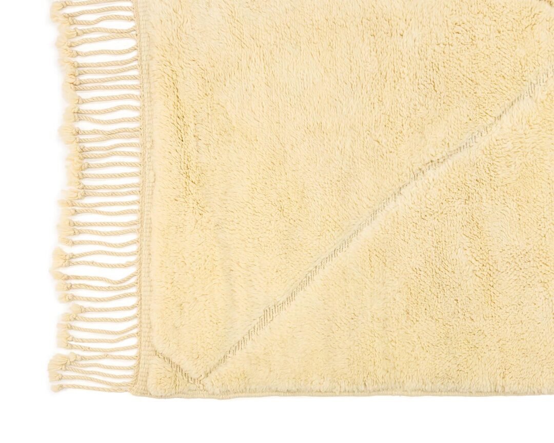 A close-up of a cream-colored, rectangular rug showcases fringed edges on two sides and features an elegant diagonal seam pattern.