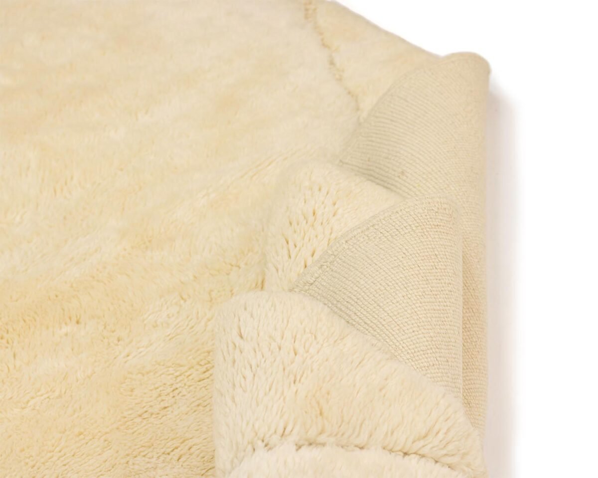 A close-up of a cream-colored, plush fabric rug showcases its intricate details, with a folded corner revealing the textured underside and hints of luxurious elegance.