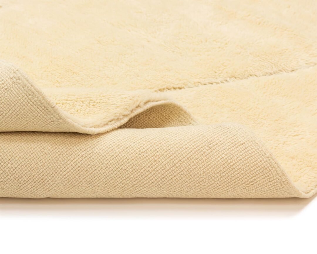 Close-up of a folded beige throw reveals its soft, fuzzy texture on top and woven underside.