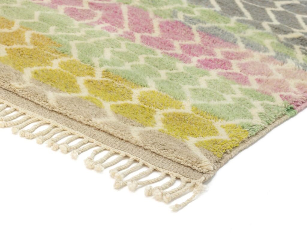 Close-up of a luxurious, hand-knotted rug featuring a geometric pattern in pastel shades. Fringes are artfully visible on one edge, adding to its Moroccan charm.