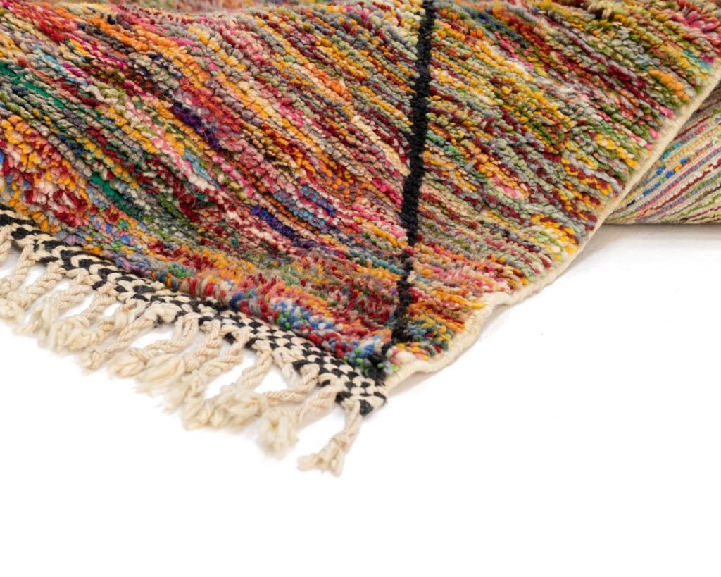 A close-up of a vibrant, textured rug showcasing lively streaks of red, yellow, green, and blue yarn with a fringe edge. The dynamic colors bring an energetic touch to any space.