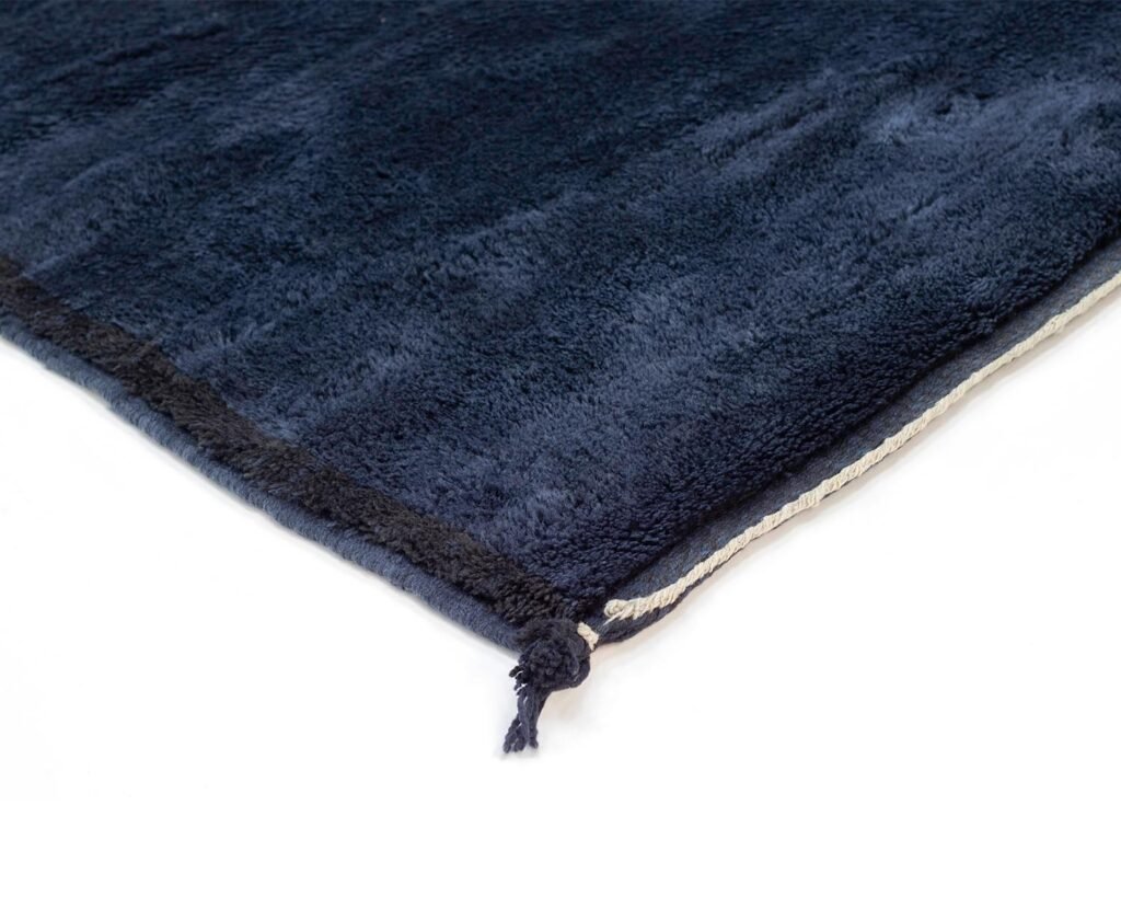 Dark blue textured rug with white fringe on the edge, shown on a white surface.