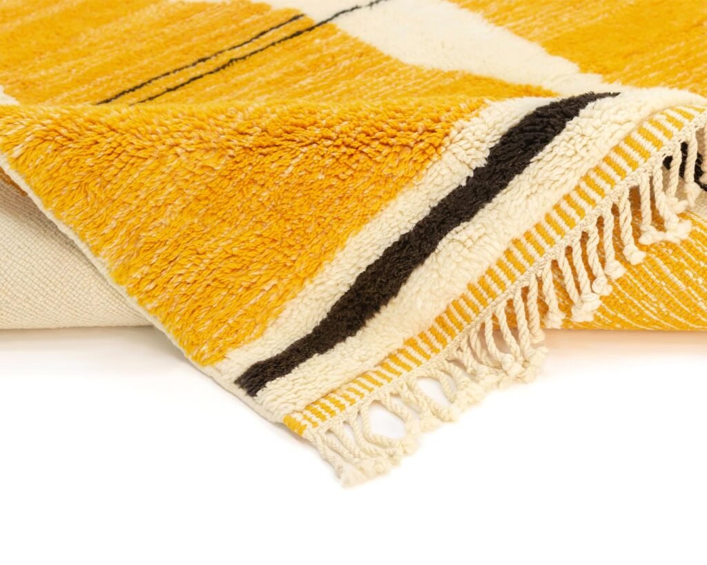 A yellow, black, and white woven textile featuring fringe on the edges lies partially folded, displaying its pattern and texture.