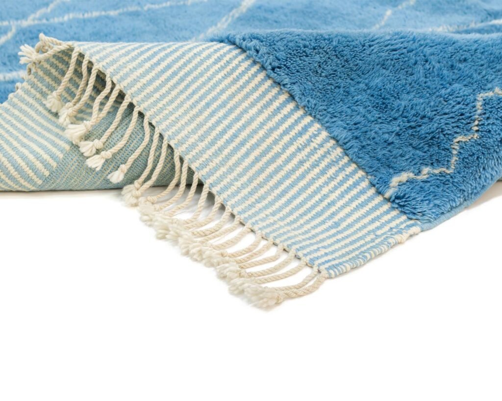 A blue and white fringed rug, crafted with luxury in mind, is partially folded to reveal a vibrant striped underside.