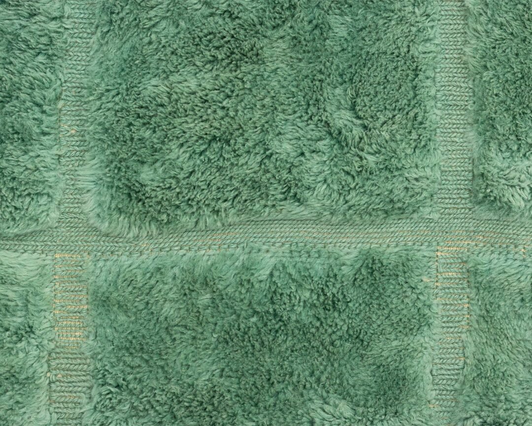 Green Moroccan hand knotted rug featuring a subtle abstract pattern that mimics organic shapes, close-up texture