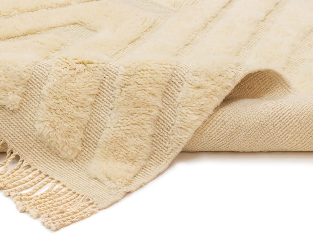 A beige textured rug with fringe edges showcases a stylish mix of plush and woven patterns.