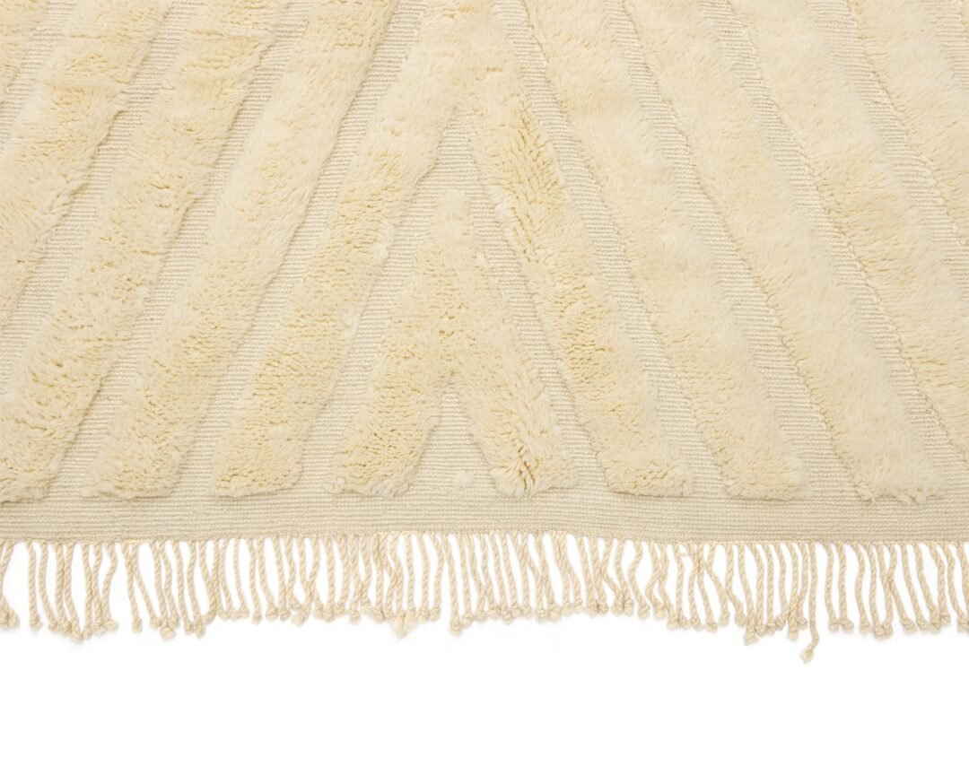 A beige textured rug showcases a geometric pattern and elegant fringe along the edge.