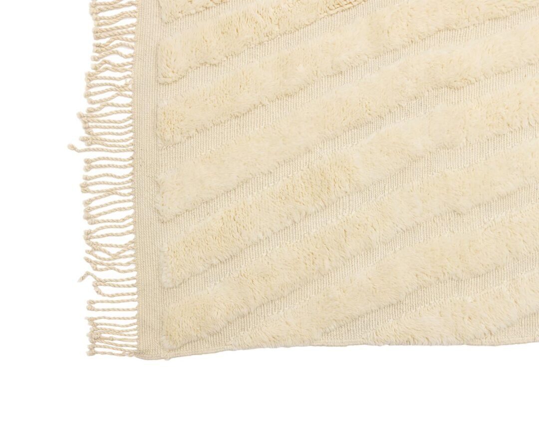 A beige rug featuring a diagonal striped pattern and fringed edges on one side adds elegance to any room.