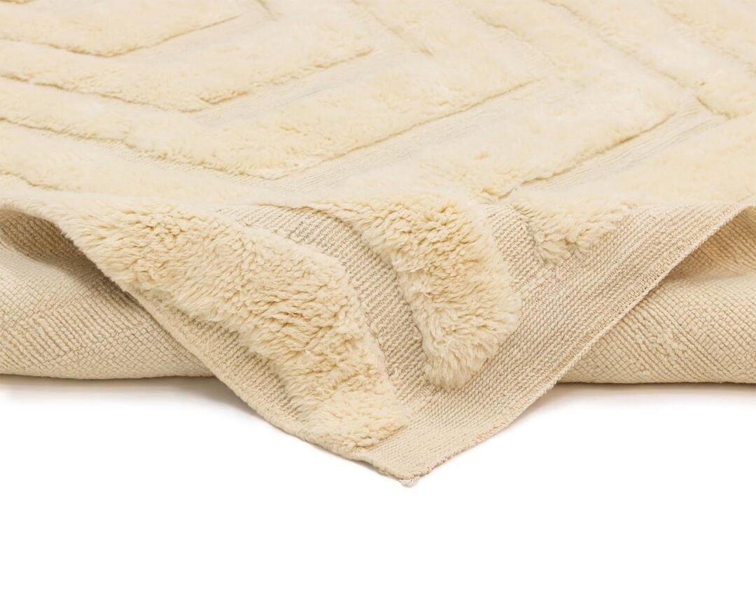 Close-up of a cream-colored, textured textile showcasing a fluffy, soft pattern, neatly folded at the corner on a flat surface.