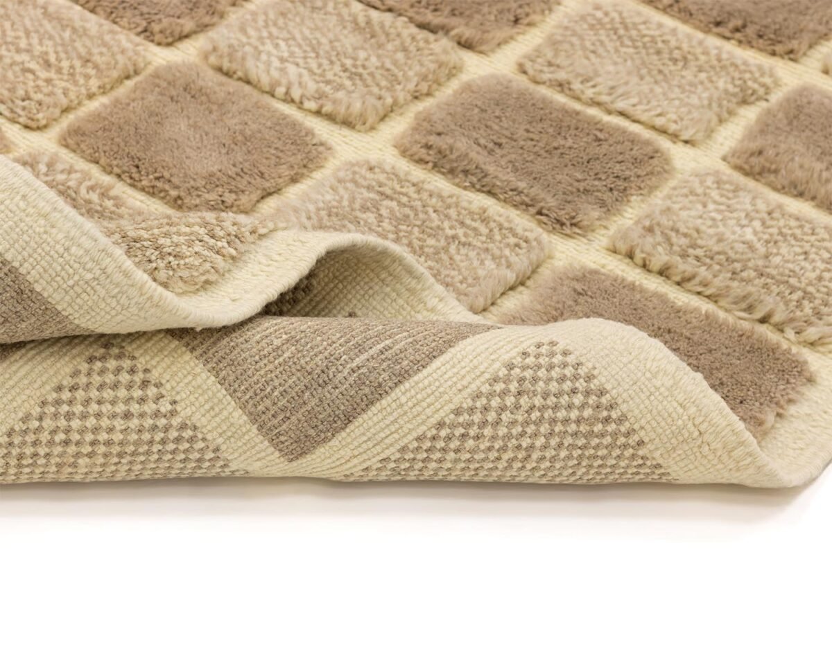 A close-up of a beige and brown checkered rug with a textured, plush surface, gently folded at the corner to reveal its cozy thickness.