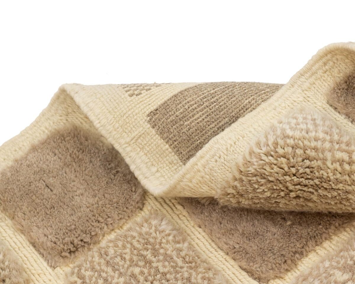 Beige and light brown checkered rug with a textured, plush surface adds a cozy touch. Its slightly folded at one corner against a white background, enhancing its elegant simplicity.