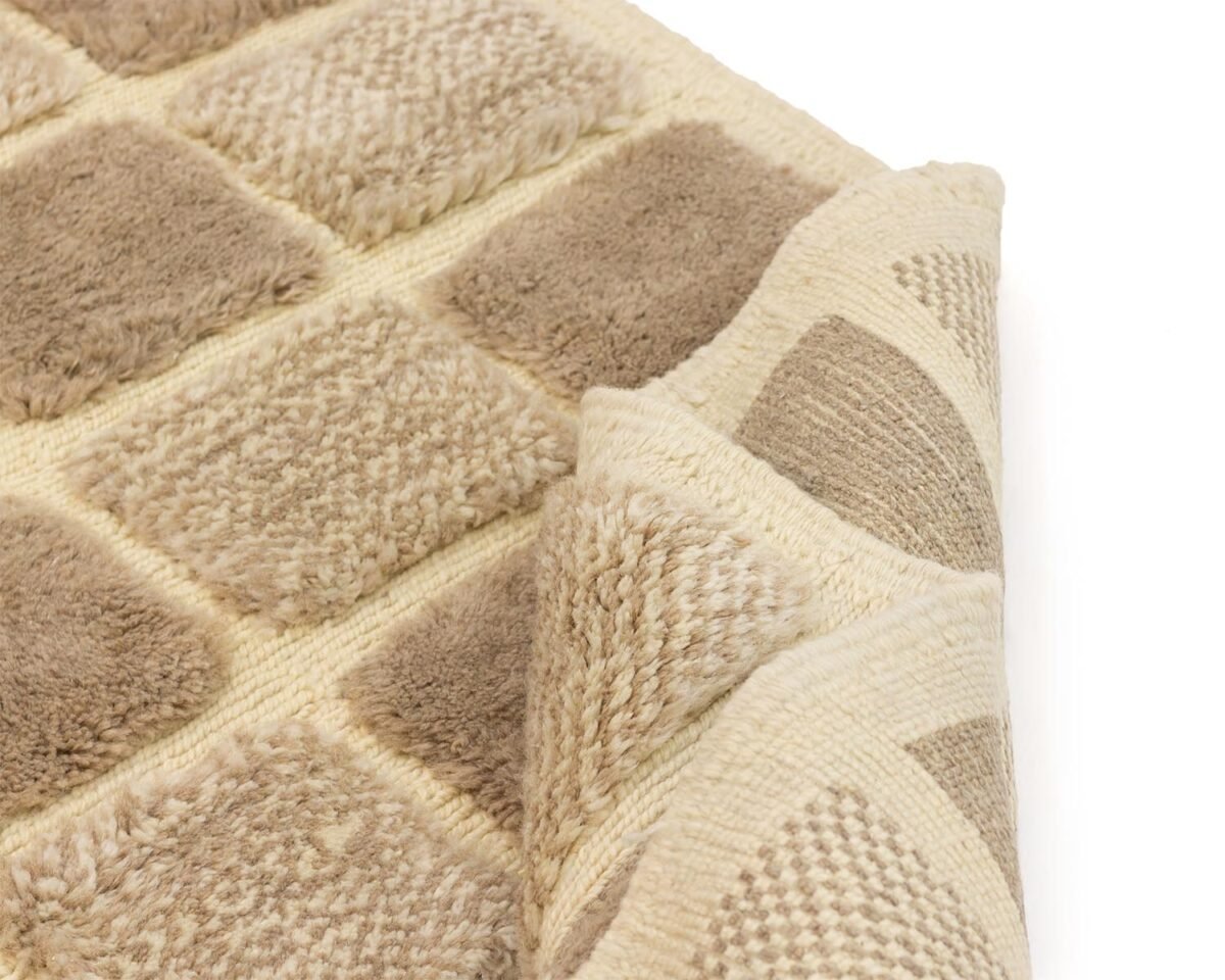 A close-up of a beige and brown textured rug with a checkered pattern, beautifully highlighting its intricate design, with one corner gently folded over.