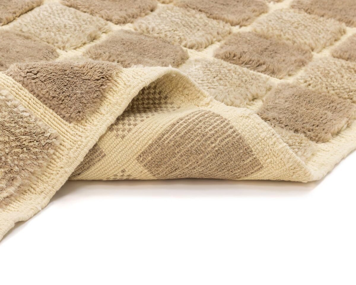 A beige and brown checkered rug with a textured surface is partially folded, revealing its intricate weave.