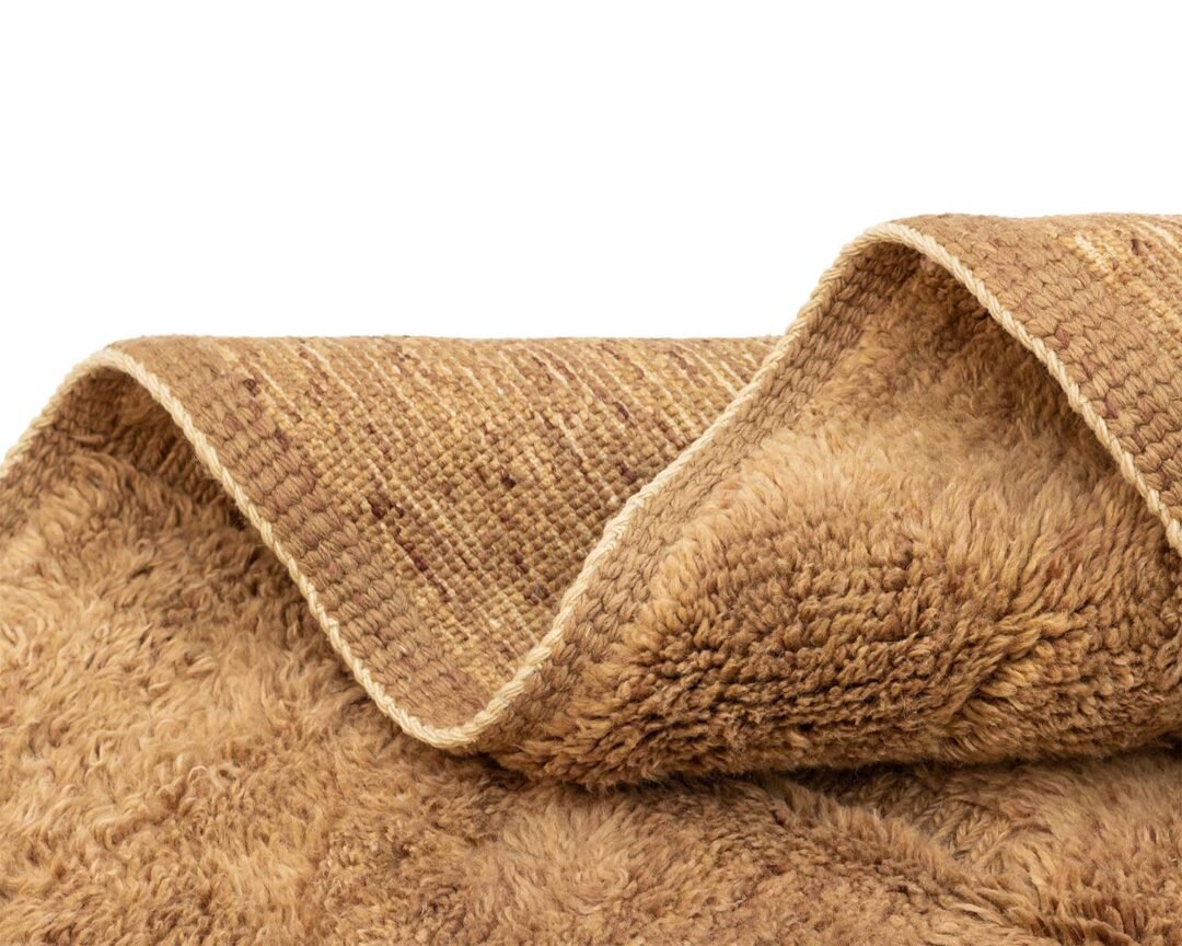 Close-up of a folded beige woven textile with a shaggy texture on one side and a velvety surface on the other, perfect for adding a touch of coziness to any room.