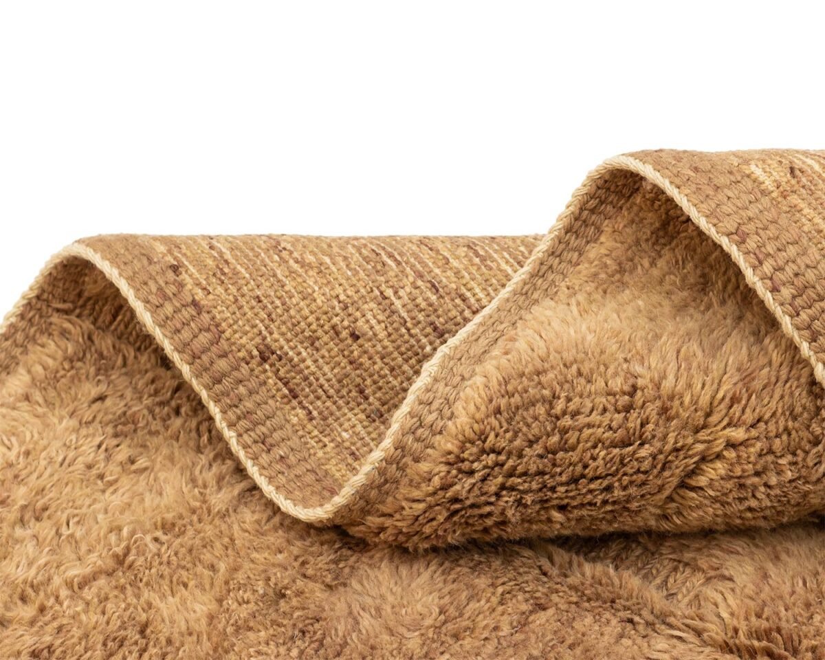 Close-up of a folded beige woven textile with a shaggy texture on one side and a velvety surface on the other, perfect for adding a touch of coziness to any room.