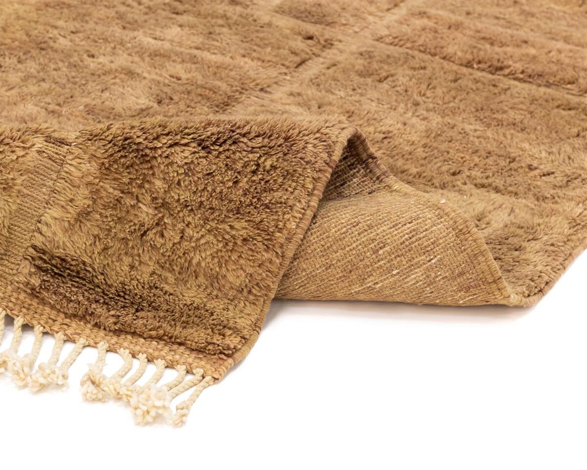 A woven, brown textured rug with fringe on one end is elegantly folded back, revealing its intricate reverse side.