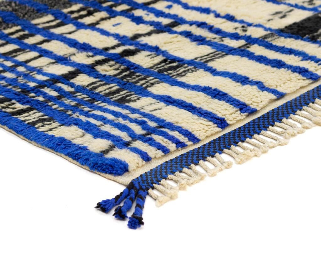 Close-up of a handmade home decor masterpiece: a blue, black, and white patterned rug corner with elegant fringes, showcasing the intricate craftsmanship of luxury rugs.