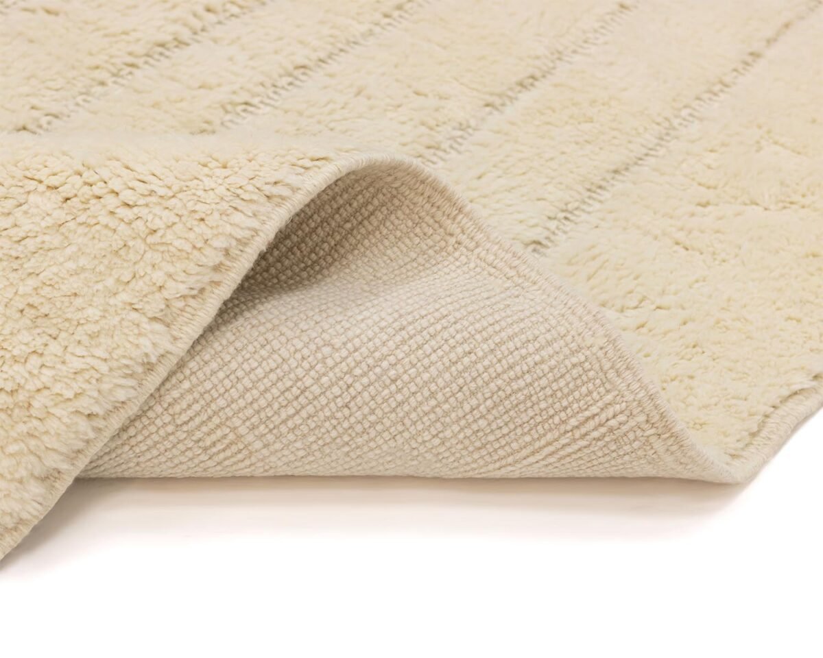 Close-up of a beige, fluffy rug with one corner flipped to reveal its intricate, textured underside and soft fibers.