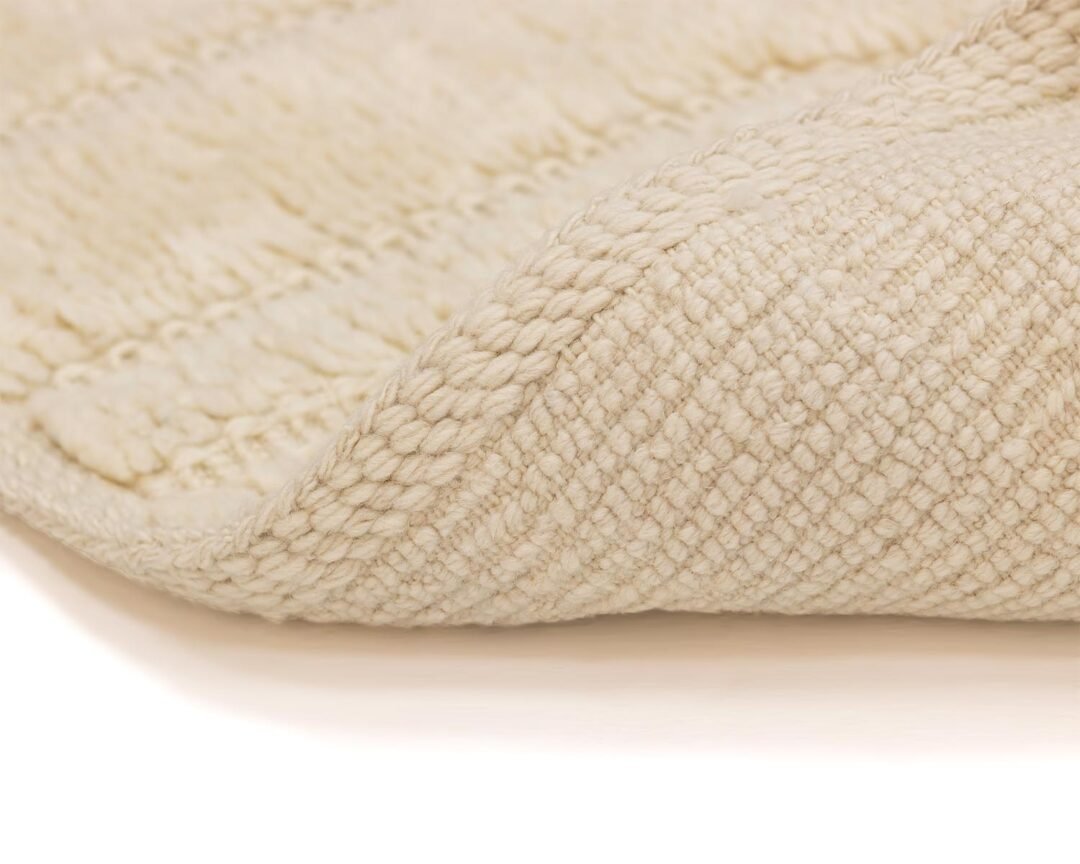 Close-up of a folded, textured beige fabric with a woven pattern, highlighting its intricate detailing and plush fibers.