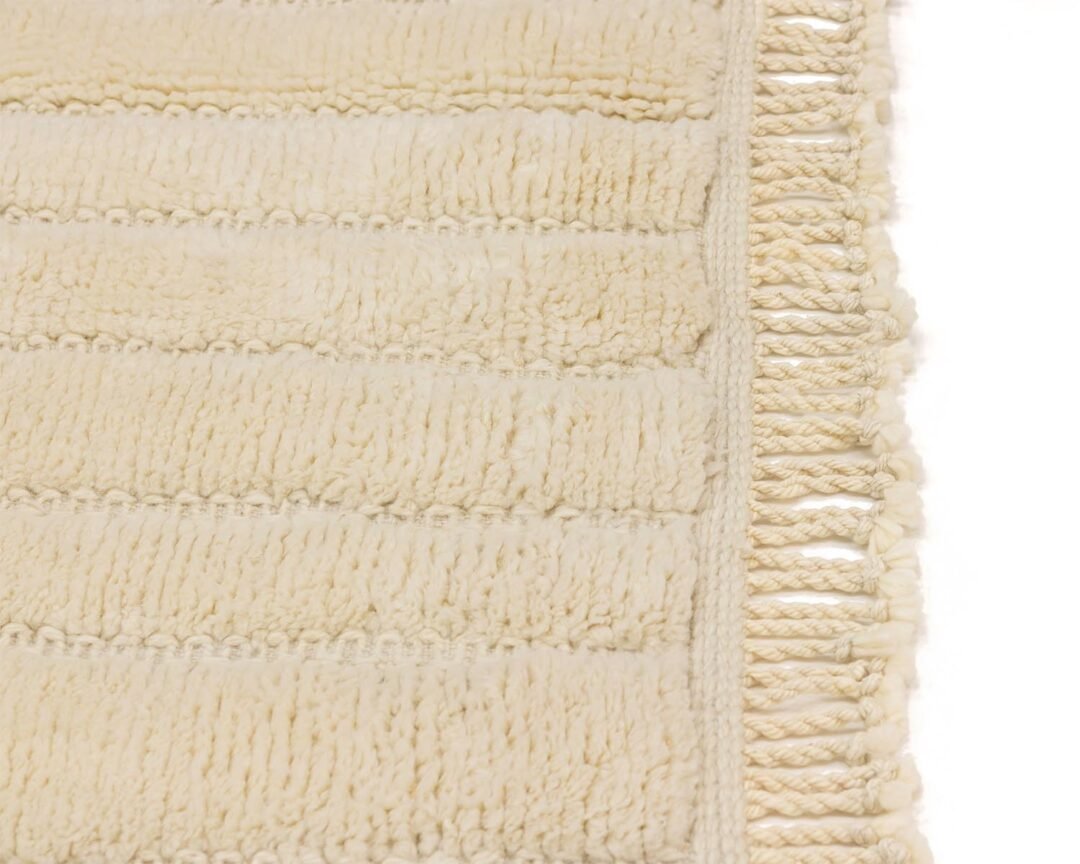 A close-up view of a textured beige rug showcasing elegant horizontal stripes and a fringed edge on the right.