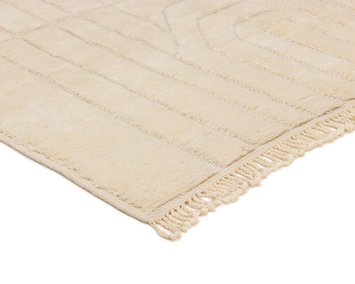 A corner of a beige rug with a subtle geometric design and fringed edges, perfect for adding a touch of style to any room.