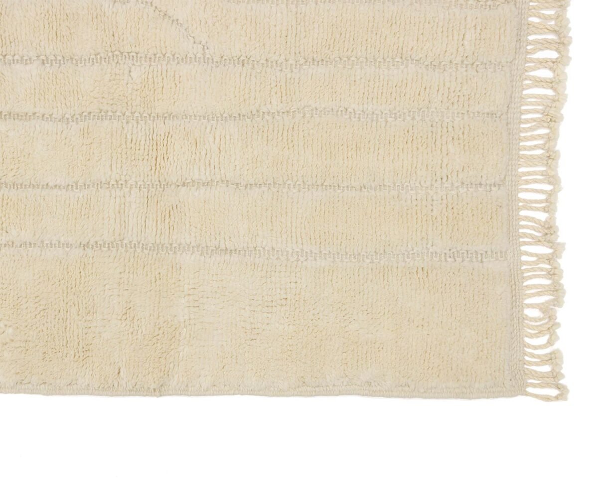 Close-up of a beige rectangular rug featuring a fringe along one edge and a subtle striped texture, adding an elegant touch to any space.