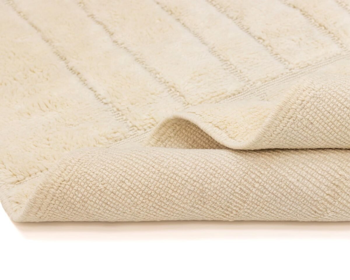 A close-up of a folded beige bath mat reveals its textured underside and ribbed surface, offering both style and comfort in your bathroom.