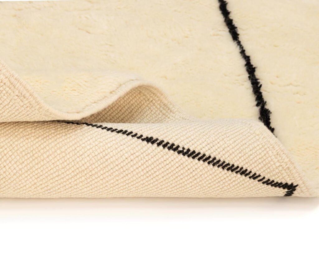 A close-up of a folded beige carpet features a striking black diagonal line that highlights the intricate weave and craftsmanship on the underside.