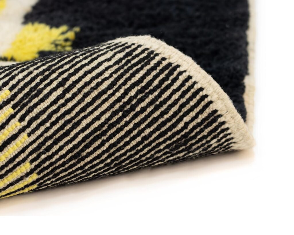 Close-up of a rolled edge of a luxury rug featuring black and white stripes with sections of yellow and black areas.