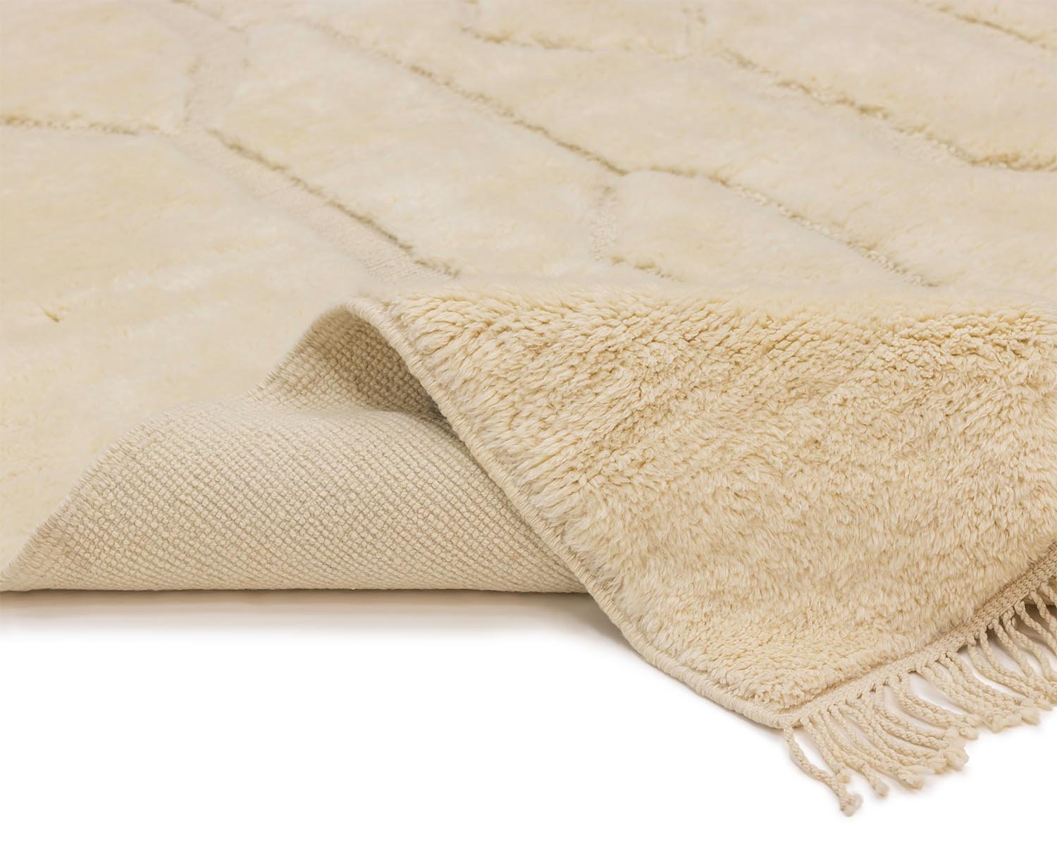 Close-up of a folded beige luxury rug with frayed edges, showcasing the intricate texture and layered construction reminiscent of a hand-knotted Moroccan style.