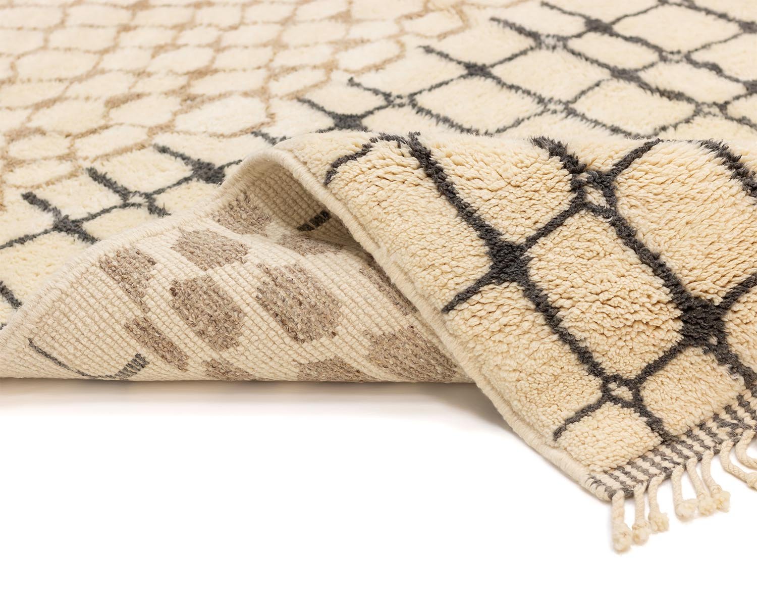 A close-up of a beige rug showcasing a black geometric pattern, partially folded to reveal its fringe and reverse side with a more subtle design.