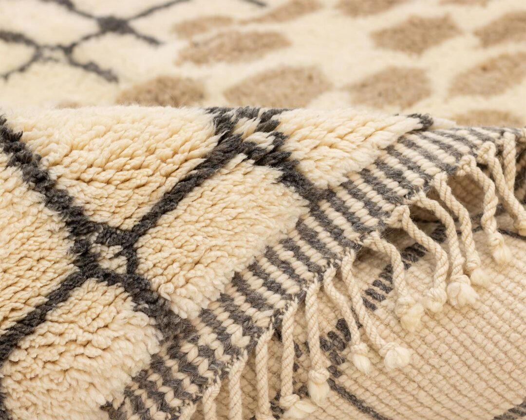 This Moroccan rug offers a close-up view of its beige and black geometric pattern with fringed edges. The hand-knotted design highlights a textured, fluffy surface, embodying luxury at every glance.