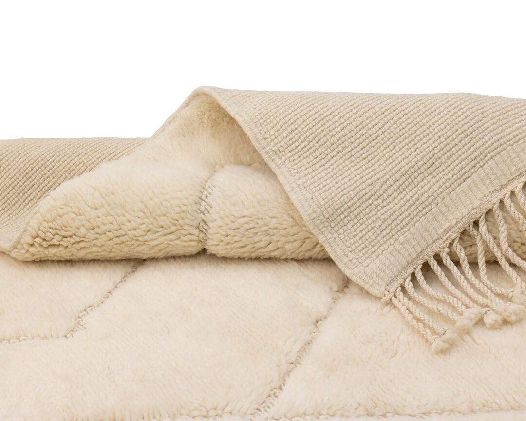 A beige, layered wool throw features a textured surface and fringed edge.