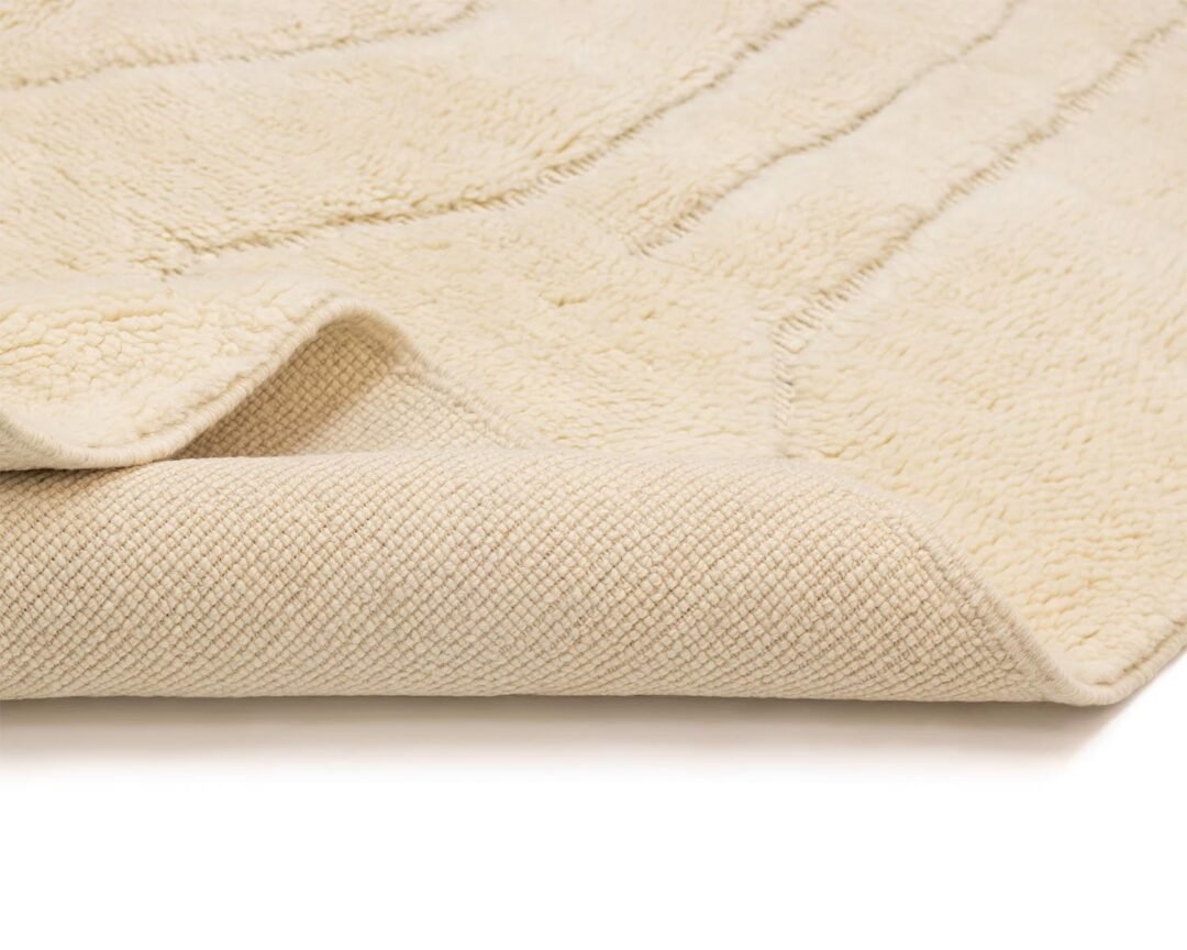 A close-up of a folded cream-colored textured rug with its intricate weave visible on the underside.